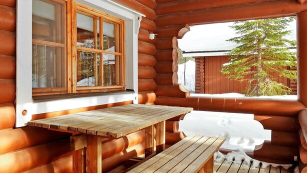 Una baita di legno con una panchina e una finestra che si affaccia su un paesaggio innevato.