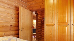 Camera da letto in una baita di legno, con un letto, pareti in legno e un'ampia porta di legno.