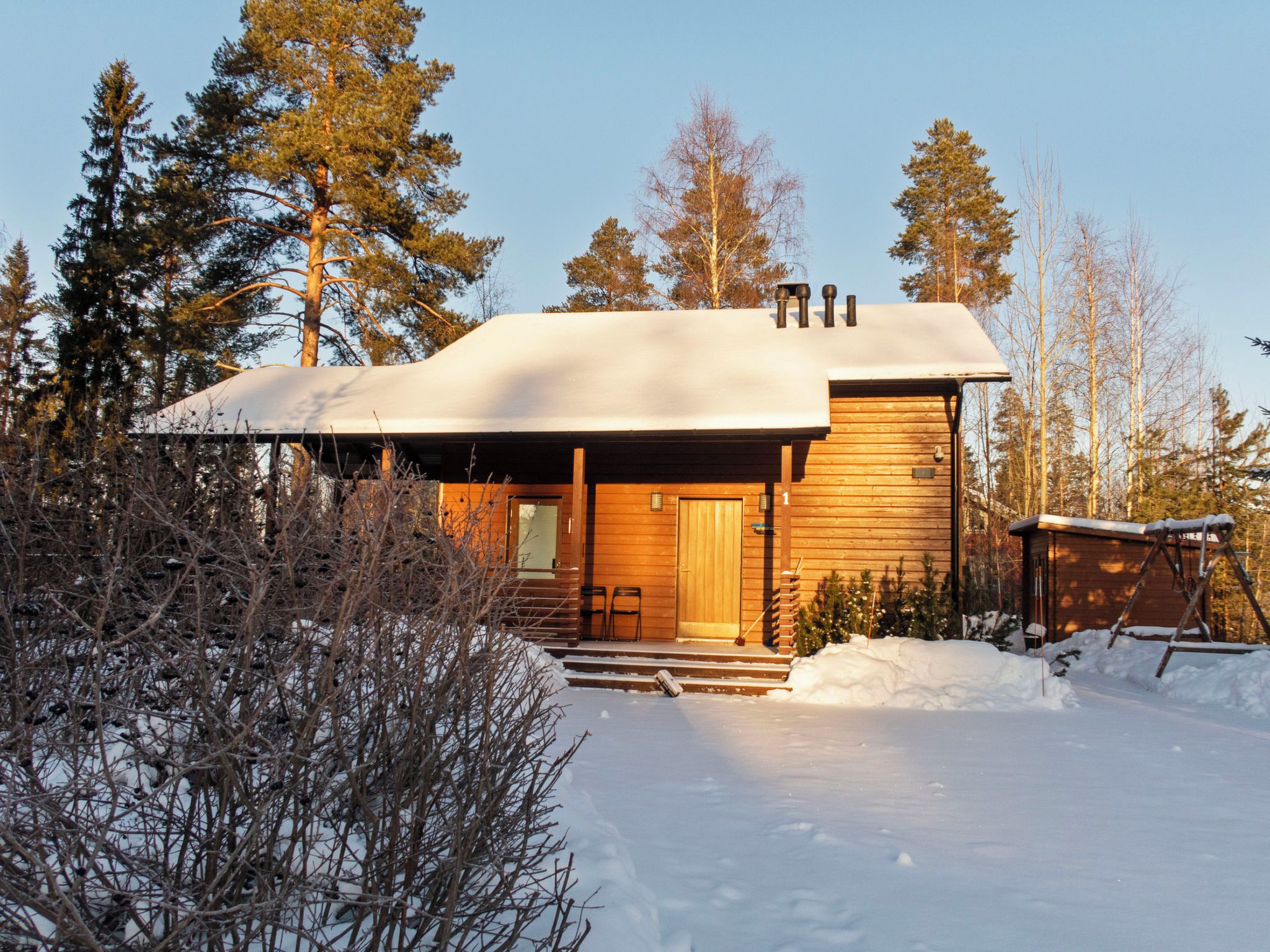 Eine Holzhütte mit überdachter Veranda, umgeben von Schnee und Bäumen.