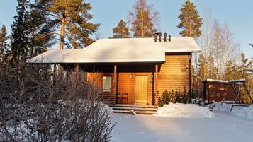 Une cabane en bois dotée d’un porche abrité, entourée de neige et d’arbres.