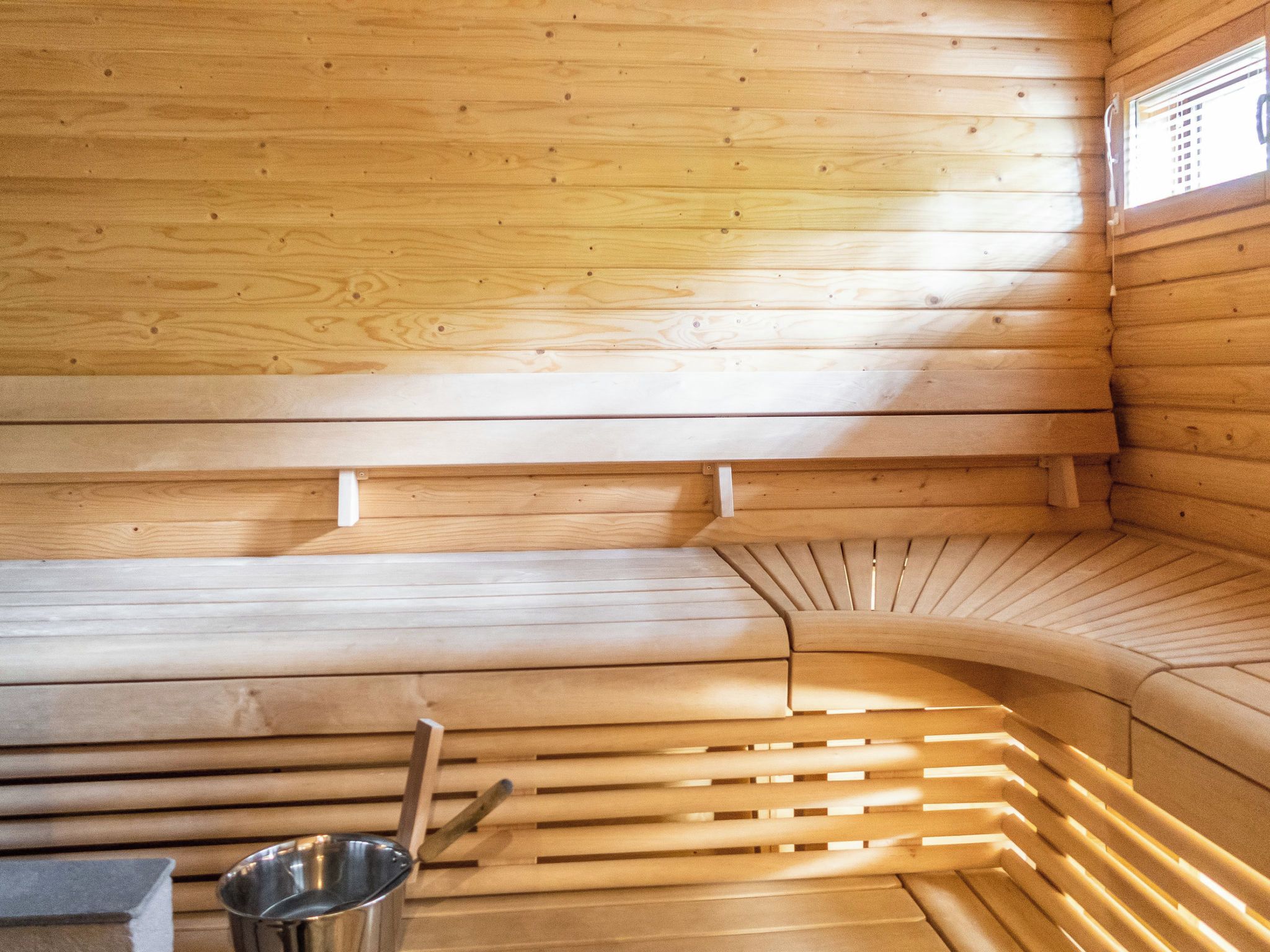 Un sauna avec des murs et des bancs en bois, un seau en métal et des bancs à lattes.