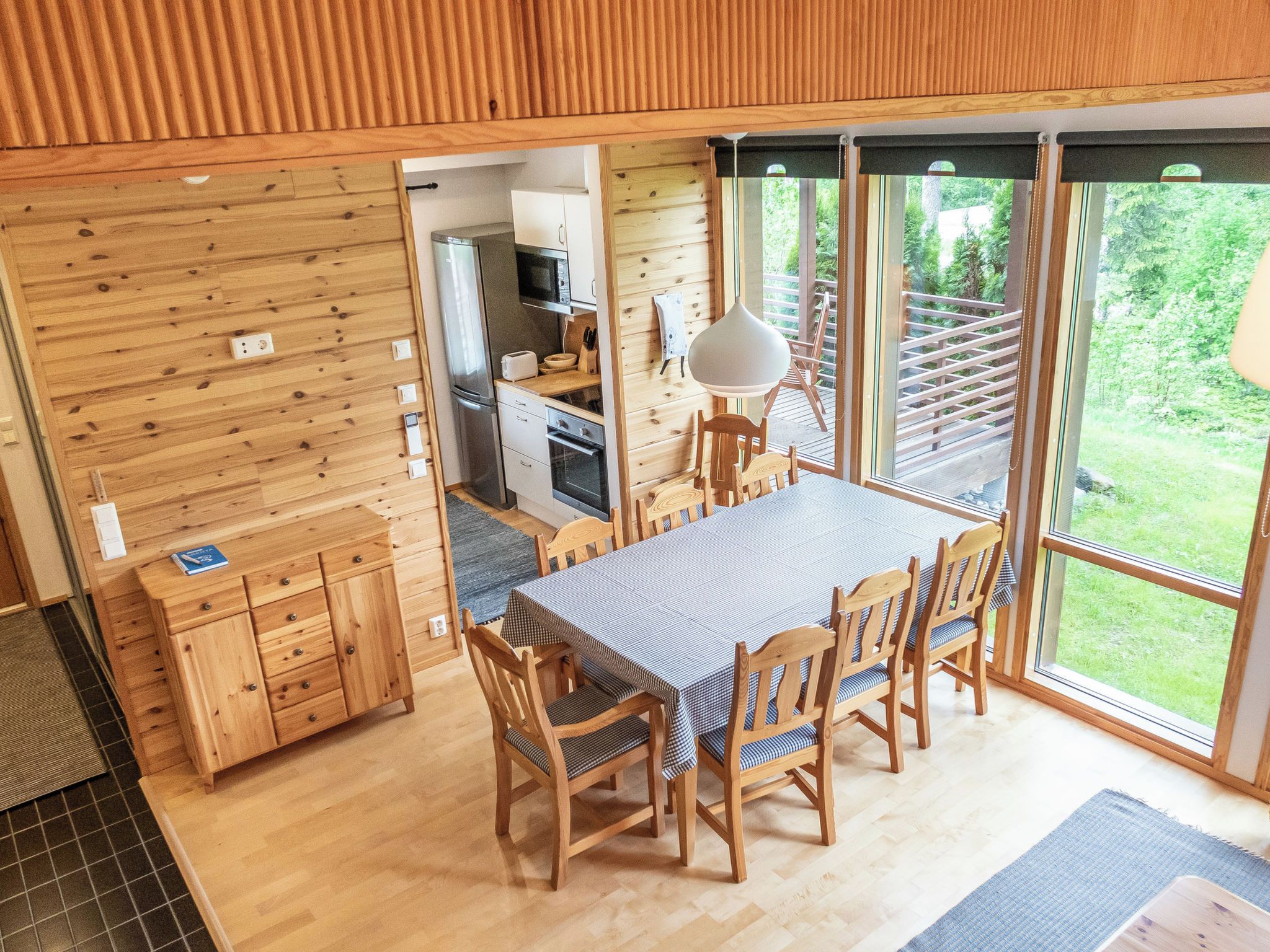 Un interior de madera con una mesa y sillas para comer, una zona de cocina y amplios ventanales con vistas al exterior.