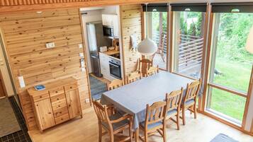 Un interior de madera con una mesa y sillas para comer, una zona de cocina y amplios ventanales con vistas al exterior.