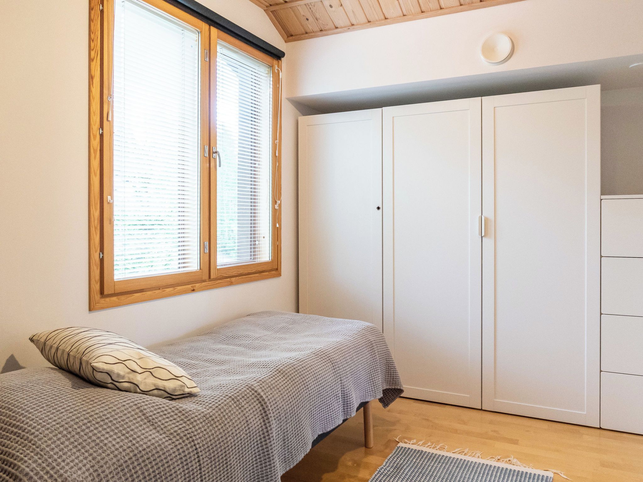 A bedroom with a bed, a wardrobe, and a window with blinds.
