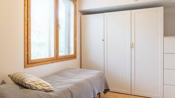 A bedroom with a bed, a wardrobe, and a window with blinds.