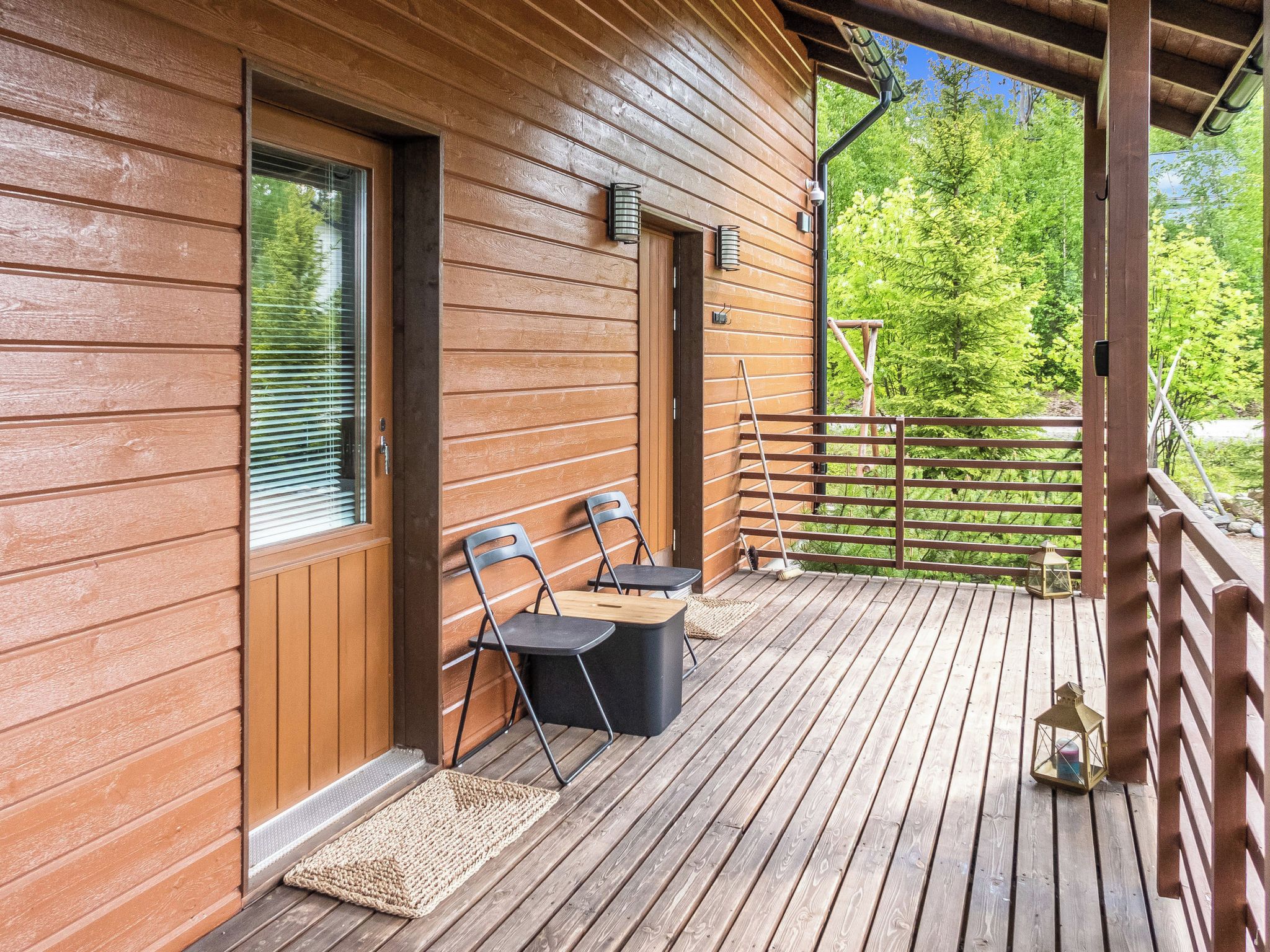A wooden deck with a covered area, two chairs, a small table, and a wooden railing.