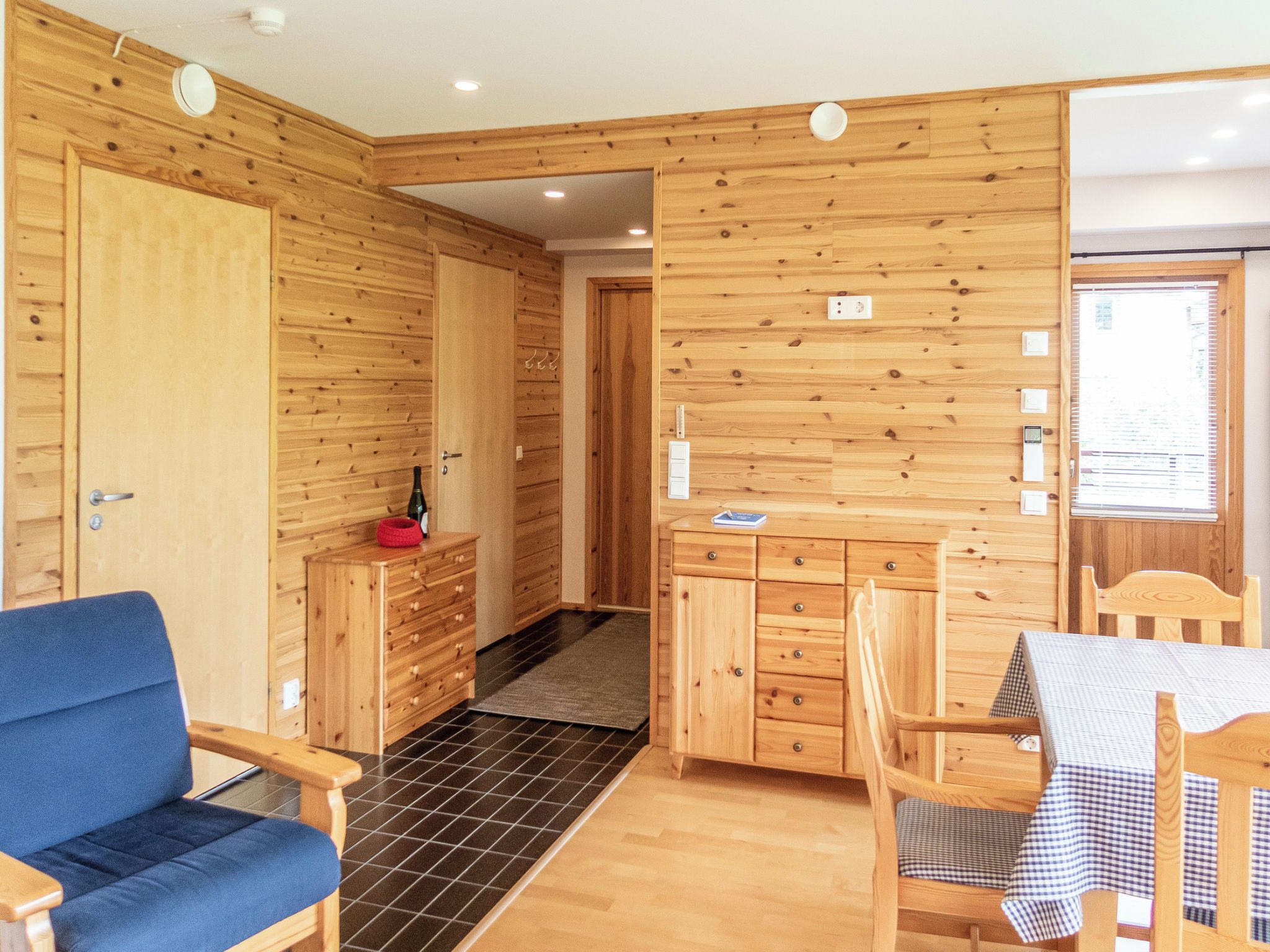 Un interior de madera con kitchenette, zona de comedor y una silla azul.