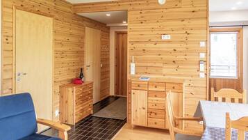 Un interior de madera con kitchenette, zona de comedor y una silla azul.