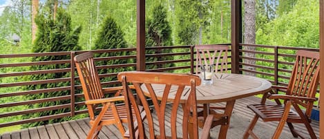 A wooden deck with a round table and four chairs, surrounded by a wooden railing, overlooking a forested area.