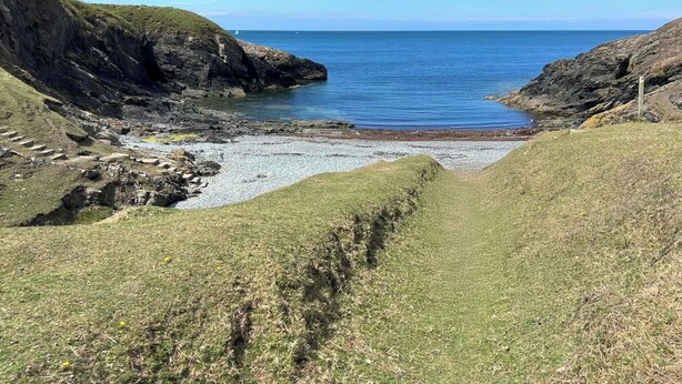 Paisaje costero con acantilados rocosos y una playa de guijarros que desemboca en el mar.