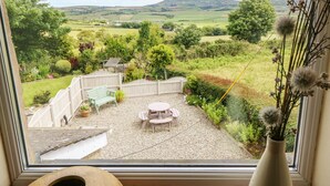 Vista desde una ventana con jardín, patio, cerca de madera y montaña al fondo.