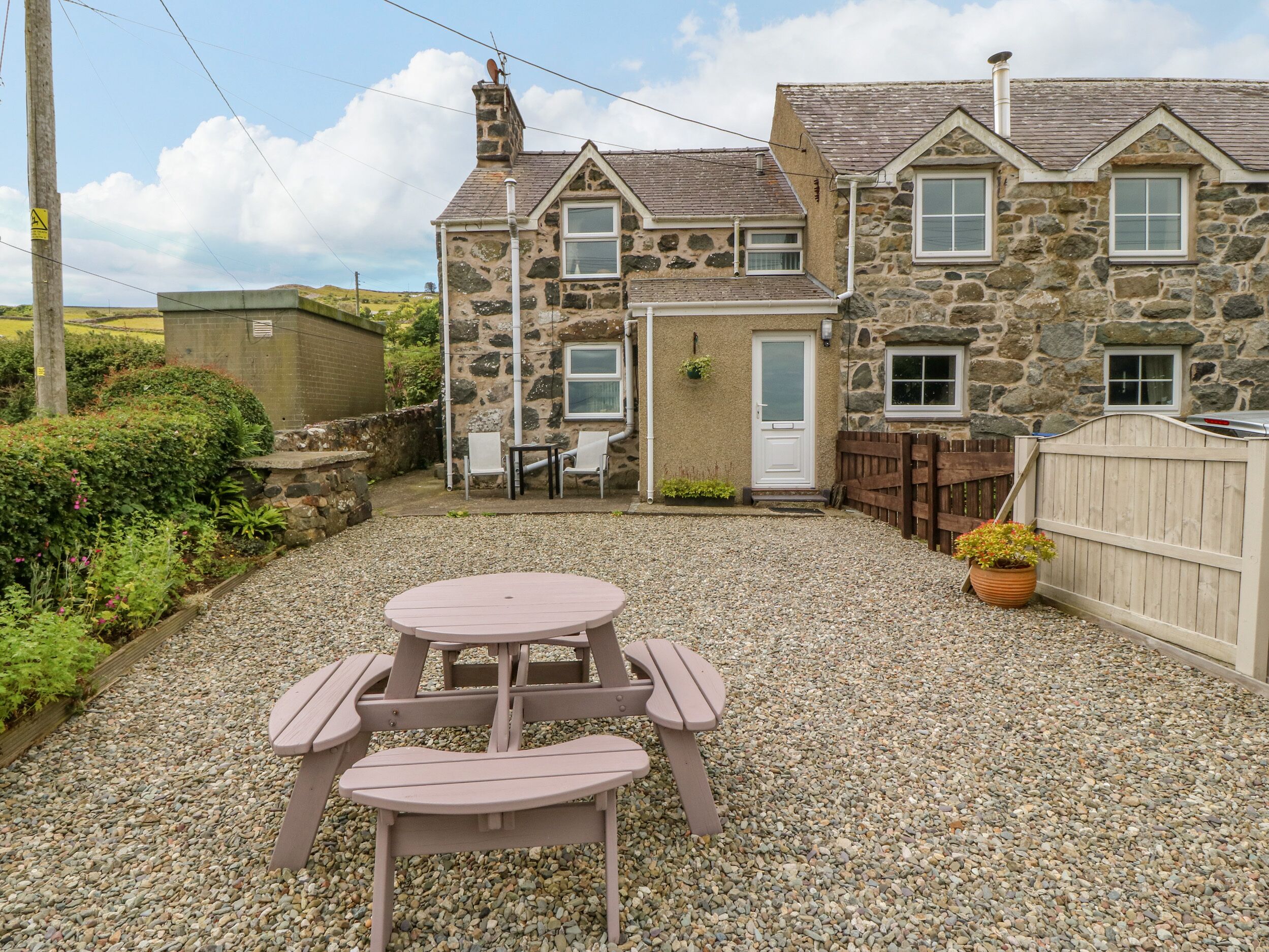 A stone house with a gravel patio, a wooden fence, and a picnic table.