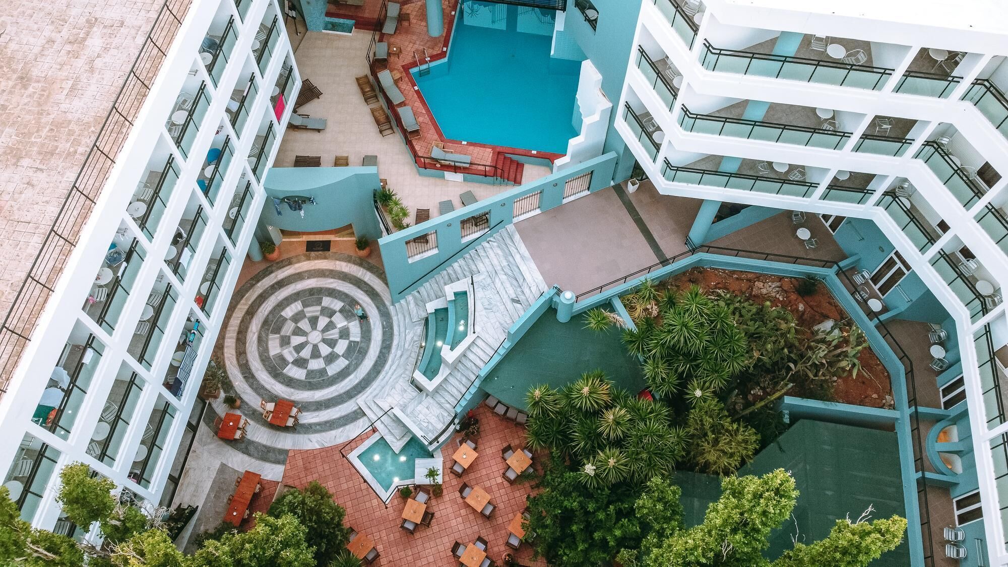 A multi-level hotel with a central pool, outdoor seating areas, and a spiral staircase.