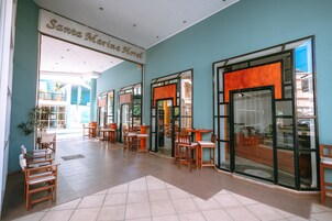 A hotel lobby with a large open space, multiple wooden tables and chairs, and glass doors leading to the outside.