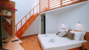 Une chambre à coucher avec un lit en bois, un bureau avec un ordinateur, une télévision, un escalier et une plante en pot.