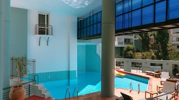 Una piscina interior con vistas a un paisaje urbano, una escalera que conduce a un balcón y un jarrón grande junto a la piscina.