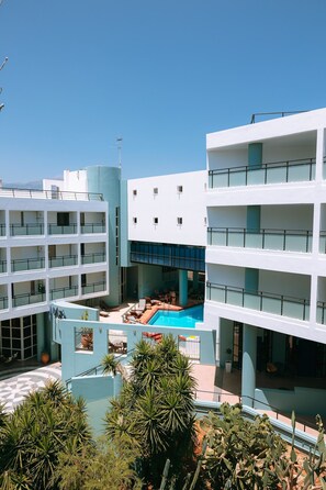 A multi-story hotel with a central courtyard featuring a swimming pool, surrounded by lush greenery and modern architecture.
