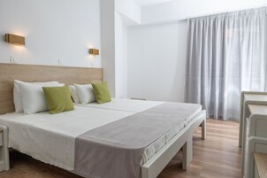 A modern hotel room with a large bed, two bedside tables, a wooden headboard, and a large window with curtains.