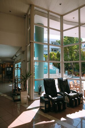 A spacious lobby with large windows, a reception desk, and massage chairs. - Santa Marina Unique Hotel (Agios Nikolaos)