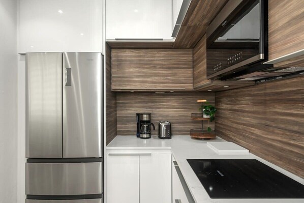 A modern kitchen with a stainless steel refrigerator, white cabinets, a black countertop, and a wooden backsplash.
