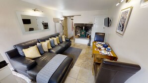 A living room with a black leather sofa, a dining table set with plates and cups, a fireplace, and a television mounted on the wall.