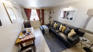 A compact living space with a dining table set for tea, a leather sofa with cushions, a small side table, and a mirror on the wall.