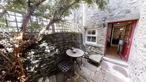 A stone wall with a small table and chairs, a bottle of wine, and a bowl of chips.