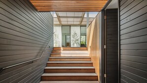 Una escalera de madera conduce a un interior moderno con una puerta de vidrio y vistas al exterior.