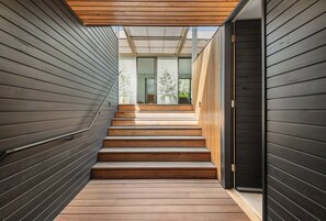 A wooden staircase leading to a modern interior with a glass door and a view of the outdoors.