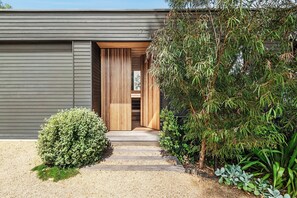 A modern building with a wooden door, a gravel pathway, and various plants.