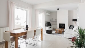 A modern living room with a white sofa, a dining table with chairs, a TV, and a fireplace. - Alluring 2BR Apartment in Marousi (Marousi)