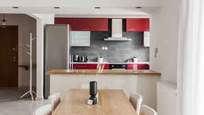 A modern kitchen with red cabinets, a wooden countertop, and a dining area with a table and chairs. - Alluring 2BR Apartment in Marousi (Marousi)
