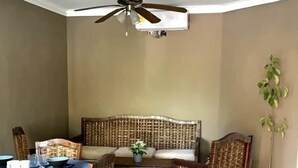 Ein Essbereich mit blauem Tischläufer, Korbstühlen, einem Deckenventilator und einem Blumentopf.