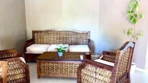 Ein Zimmer mit einem Korbssofa, zwei gleichgestimmten Sesseln und einem kleinen Couchtisch.