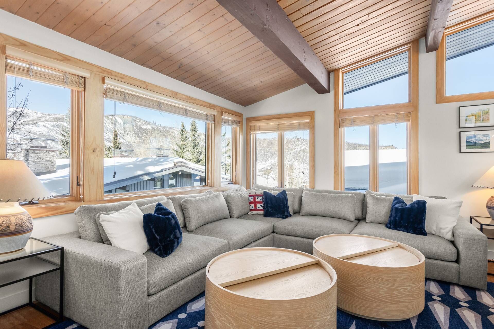 Una sala de estar moderna con un sofá modular gris, dos mesitas de madera y un ventanal con vistas a un paisaje nevado.