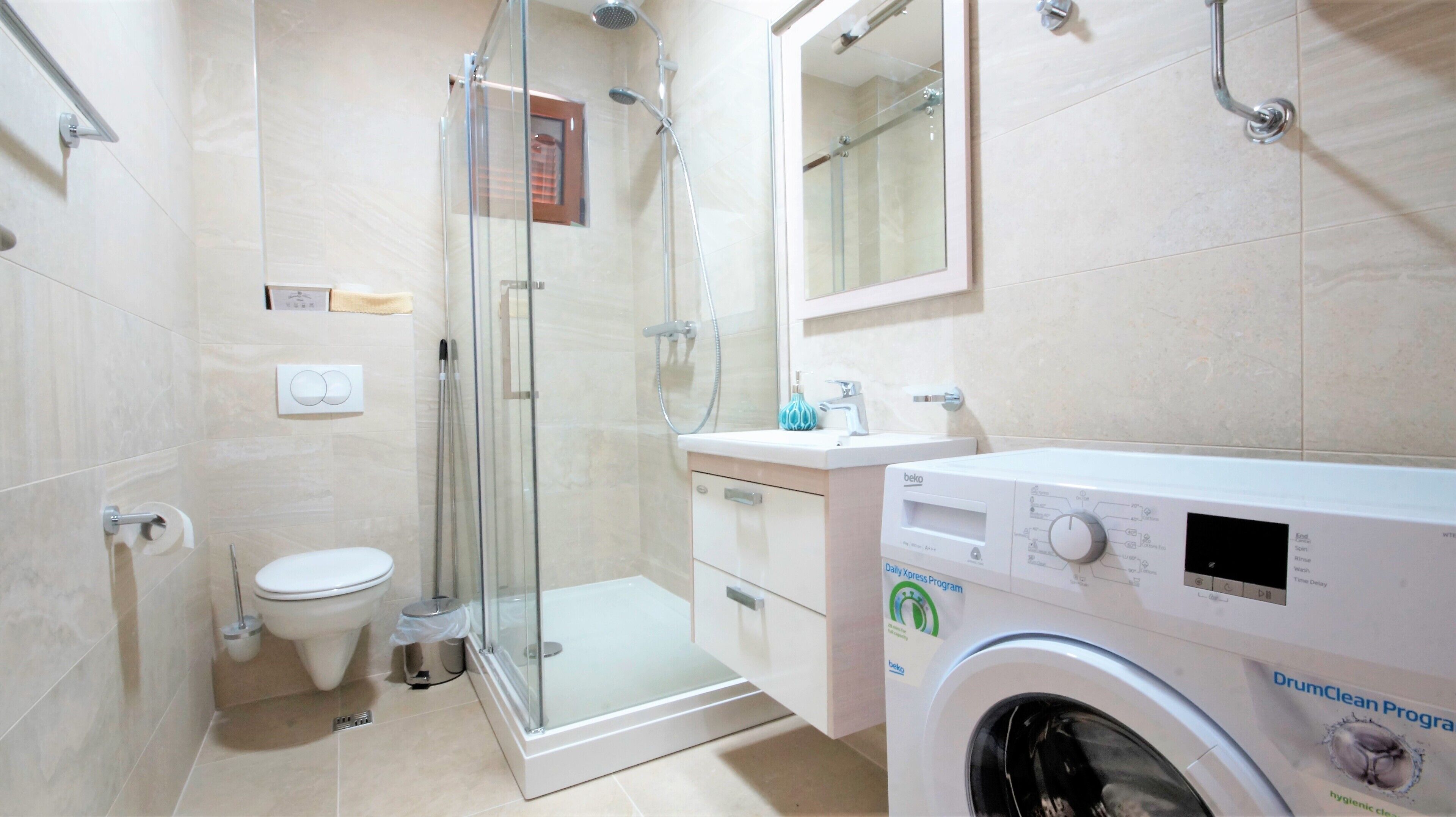 A modern bathroom with a glass-enclosed shower, a toilet, a sink, and a washing machine.
