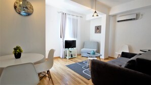 A modern living room with a sofa, a dining table with chairs, a TV on a stand, and a small rug. - Apartment IPEK (Budva)