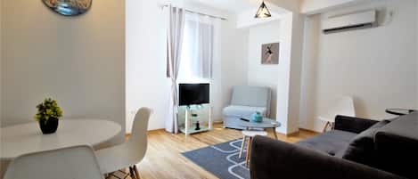 Una sala de estar moderna con un sofá, una mesa de comedor con sillas, un televisor sobre un mueble bajo y una alfombra pequeña.