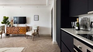 A modern kitchen with black cabinets, a wooden herringbone floor, a dining area with a herringbone-patterned table, and a flat-screen TV on the wall. - The Battersea Flat - Exquisite 2bdr Flat With Terrace (London)