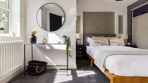 A modern bedroom with a bed, bedside table, mirror, and a radiator. - The Battersea Flat - Exquisite 2bdr Flat With Terrace (London)