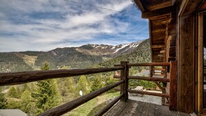 Un balcón de madera con vistas a montañas nevadas y un valle cubierto de bosque.