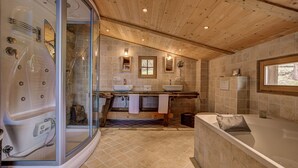 Un baño moderno con ducha envuelta en vidrio, tocador doble, bañera amplia y techo de madera.