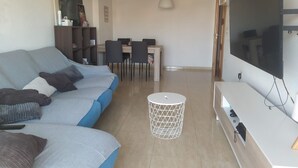 Una sala moderna con un sofá, una mesa de centro, un televisor y un comedor con sillas y una mesa.