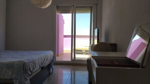 Un dormitorio con cama, escritorio y televisor. Hay una puerta corrediza que da a un espacio al aire libre.