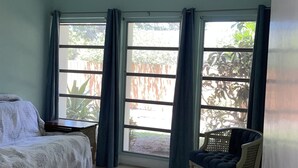 Une chambre à coucher avec un lit, une chaise, un ventilateur de plafond et de grandes fenêtres avec des rideaux.