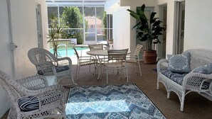 Un patio couvert aménagé avec des meubles en osier, un tapis à motifs et une vue sur une piscine et la verdure environnante.