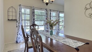 Un coin repas avec une table en bois, des chaises, un chemin de table en dentelle, un vase de fleurs et un lustre.