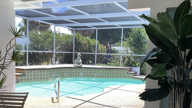 Un espace piscine doté d’une enceinte en verre, un coin salon avec un banc et une plante en pot.