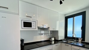 Una cocina moderna con armarios blancos, un refrigerador de acero inoxidable, un microondas, un horno, un lavavajillas y una ventana con vista al mar.