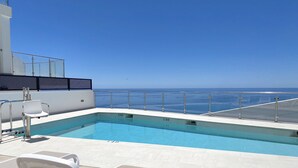 Un área de piscina con sillas de descanso y vista al océano.